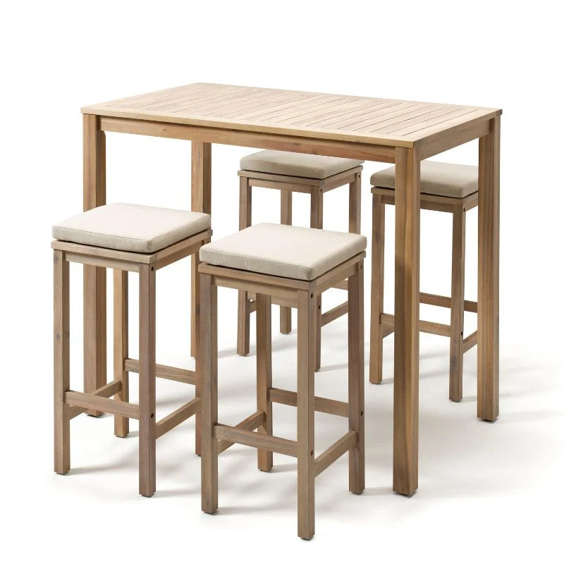 Ein helles Bar-Set aus Holz, bestehend aus einem hohen Tisch und vier passenden Barhockern mit hellen Sitzkissen. Die kompakten Hocker sind so konstruiert, dass sie sich bei Nichtgebrauch platzsparend unter die Tischplatte schieben lassen.