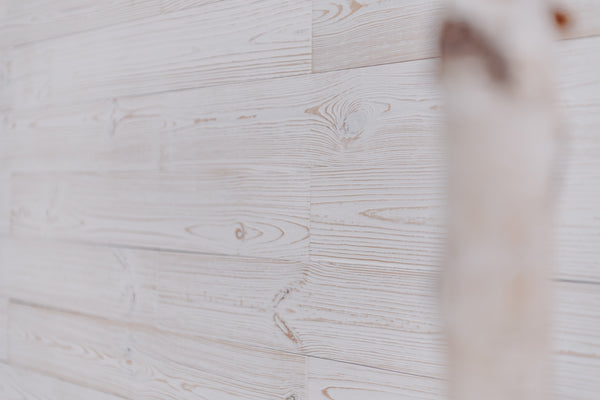 Weiße Holzpaneele an einer Wand, bei denen die natürliche Holzmaserung und die Äste dezent durch die Farbe scheinen