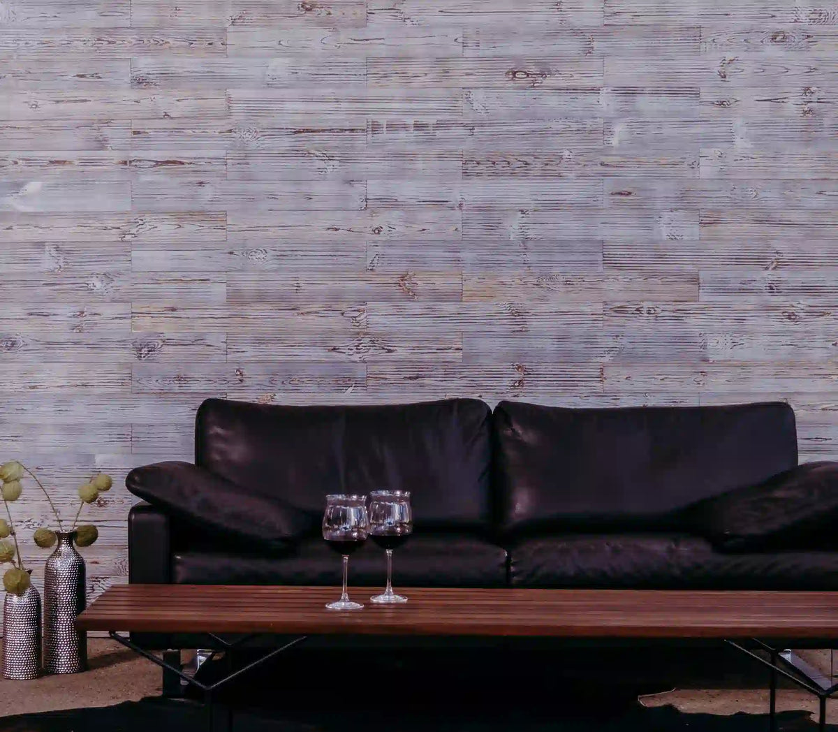 Graue Holzwand mit einem brauen Ledersofa und einem Holztisch mit zwei Weingläsern darauf