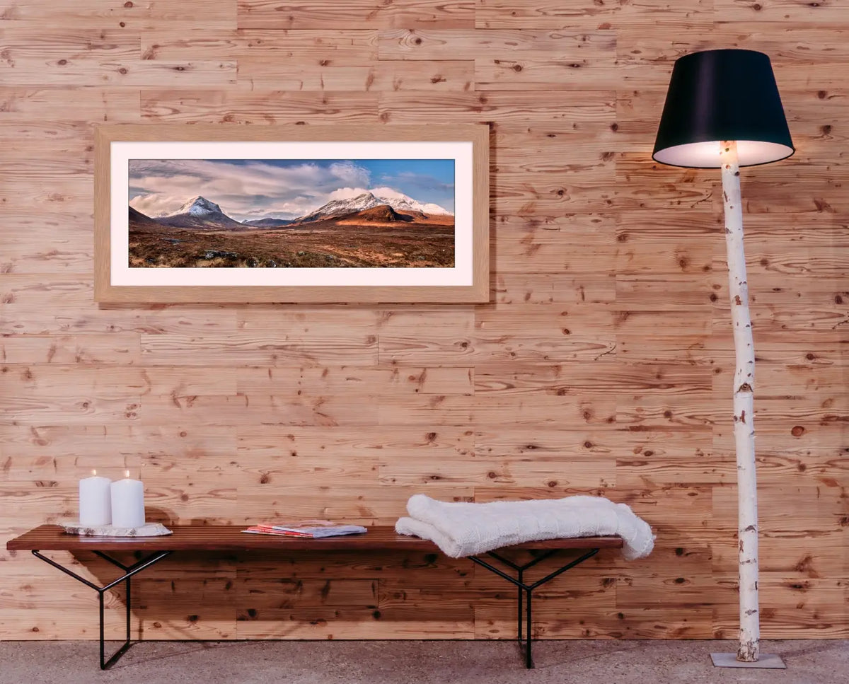 Eine moderne Stehlampe mit einem Fuß aus einem naturbelassenen Birkenstamm und schwarzem Schirm steht vor einer hellen Echtholz-Wandverkleidung. Ein gerahmtes Landschaftspanorama über einer minimalistischen Holzbank rundet das natürliche Raumdesign ab.