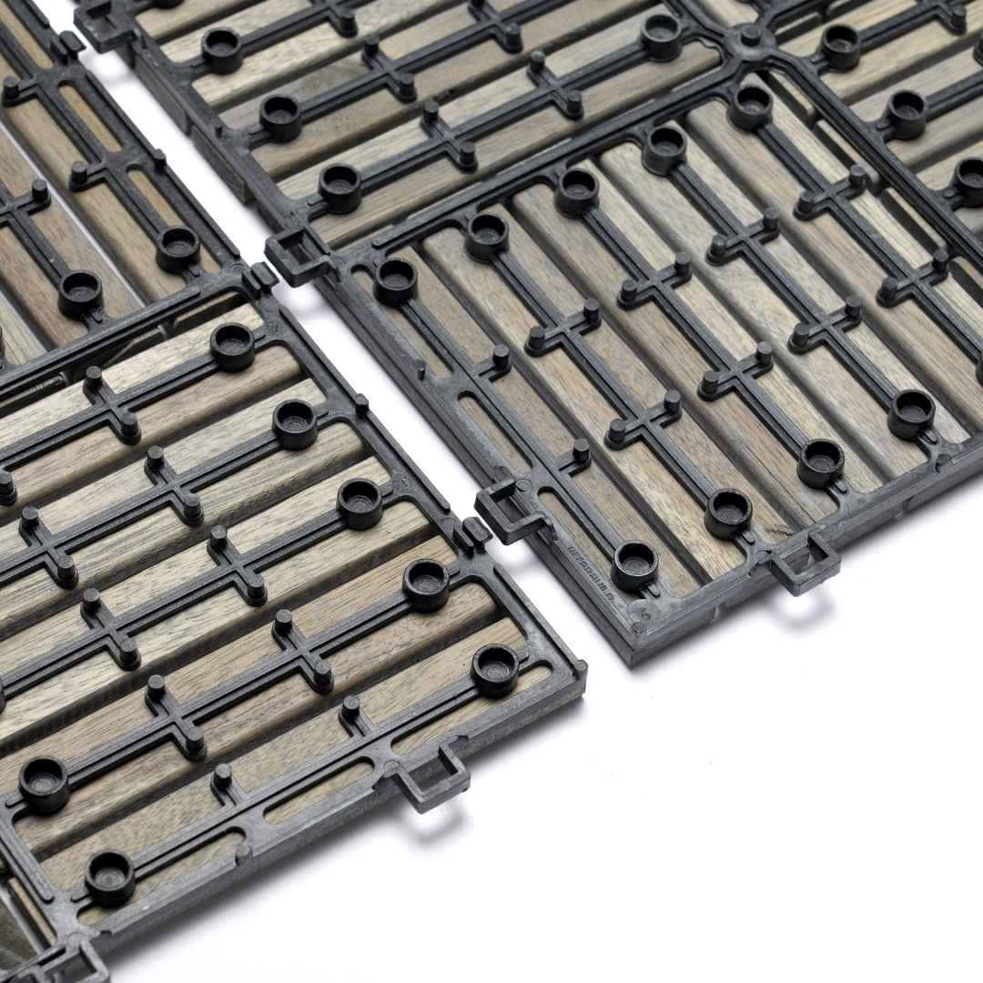 Eine Nahaufnahme der Unterseite von Holz-Klickfliesen zeigt das schwarze Kunststoff-Gitter mit integrierten Verbindungsösen. Die Konstruktion verdeutlicht das einfache Stecksystem und die Drainage-Funktion für den Außeneinsatz.