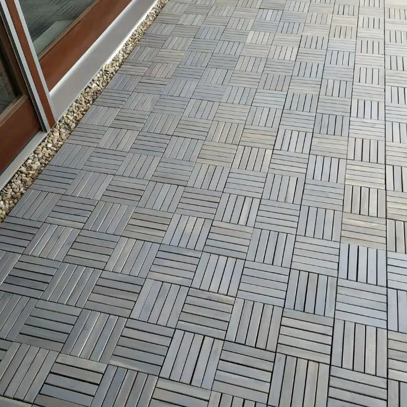 Ein langer, schmaler Balkon ist vollständig mit grauen Holzfliesen im Klicksystem ausgelegt, die ein gleichmäßiges geometrisches Muster bilden. Der saubere Abschluss zur Hauswand und die durchgehende Fläche zeigen die effiziente Verlegung auf größeren Außenbereichen.