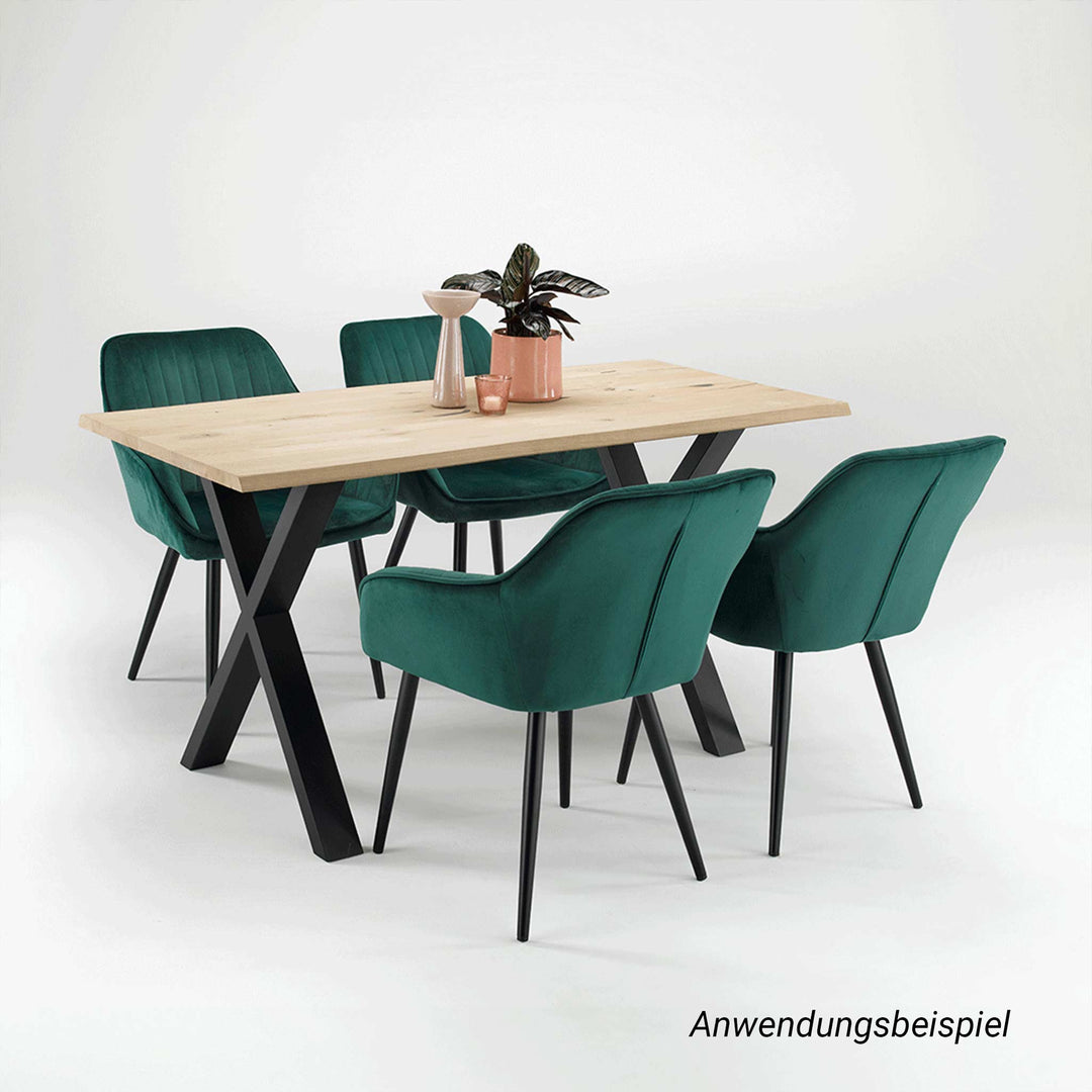 Ein gepflegter Esstisch mit makelloser, heller Massivholzplatte und schwarzem X-Metallgestell steht zusammen mit vier dunkelgrünen Samtstühlen vor einem weißen Hintergrund.