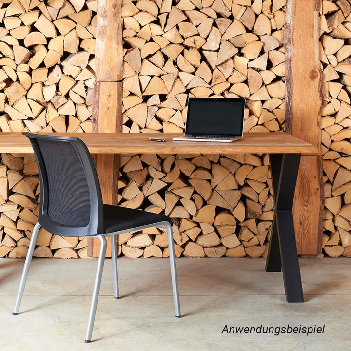 Ein moderner Schreibtisch mit massiver Holzplatte und schwarzem Metallgestell bildet einen stilvollen Kontrast zu einer raumhohen Wand aus gestapeltem Brennholz. Ein schwarzer Bürostuhl und ein aufgeklappter Laptop auf dem Tisch ergänzen diesen rustikal-modernen Arbeitsplatz.