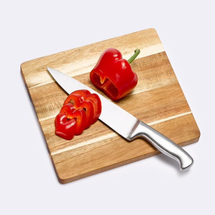 Ein Küchenmesser und eine frisch aufgeschnittene rote Paprika liegen auf einem quadratischen Schneidebrett aus hellem, klingenschonendem Holz.