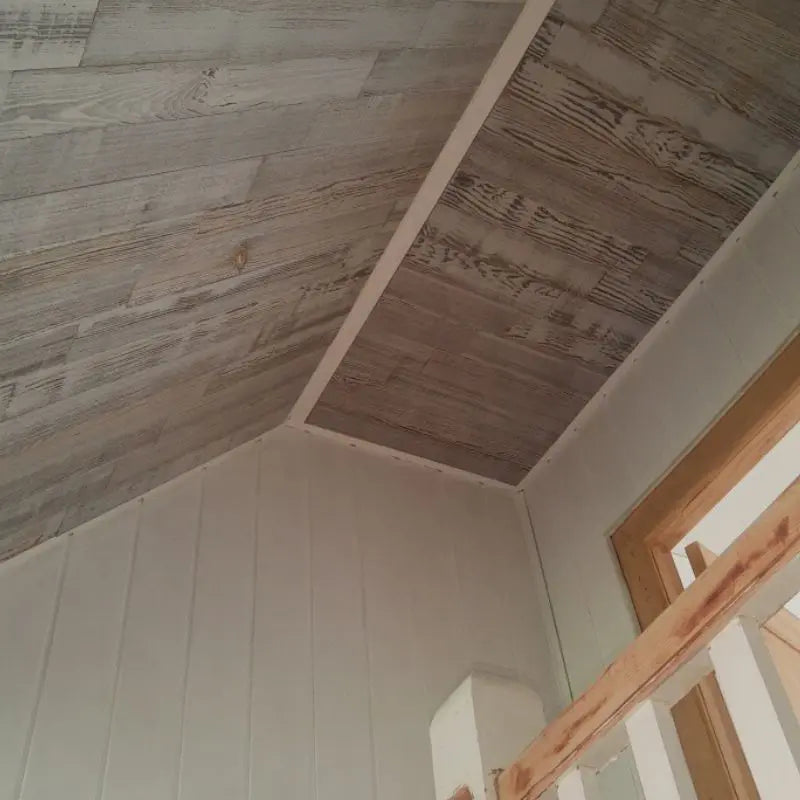 Eine Dachschräge ist mit grau lasierten Holzpaneelen verkleidet, die einen hellen Kontrast zu den angrenzenden weiß gestrichenen Wänden bilden.