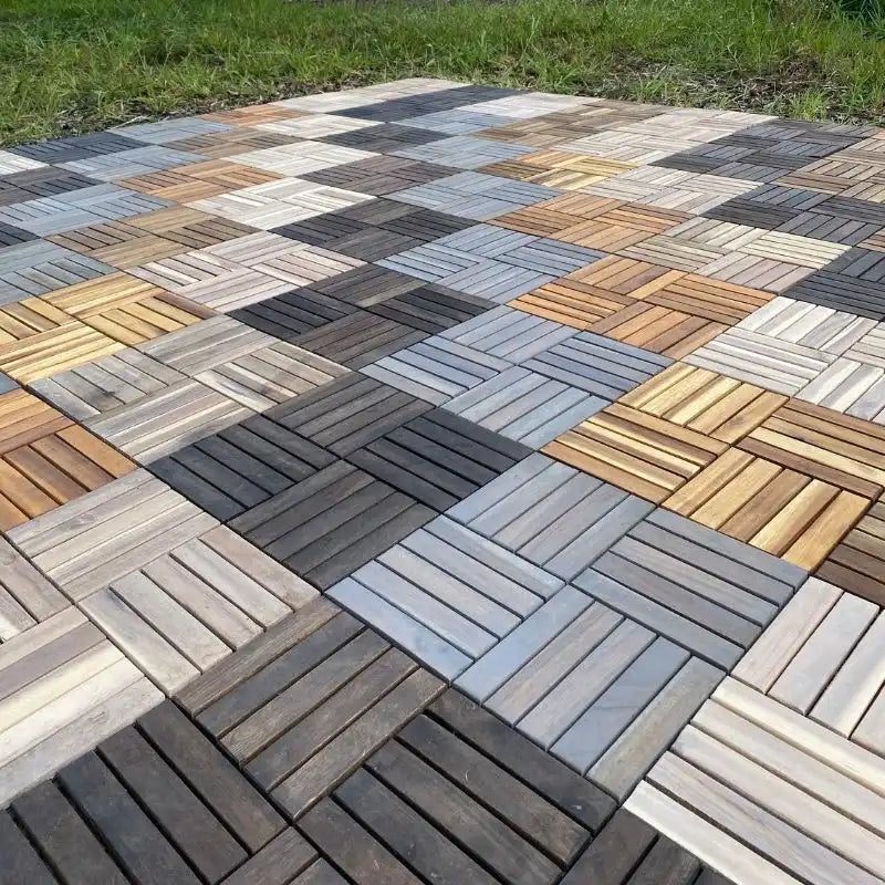 Eine großflächig verlegte Terrasse aus quadratischen Holzfliesen in verschiedenen Naturtönen, die direkt an eine Rasenfläche mit Bäumen grenzt.