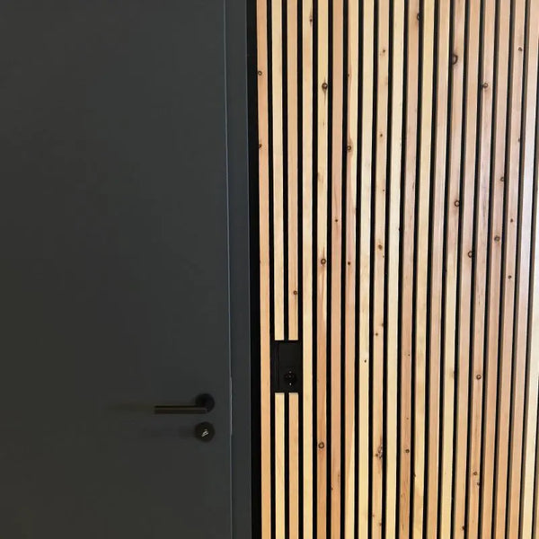 Akustikpaneele aus Zirbenholz bilden eine strukturierte Wandverkleidung direkt neben einer dunkelgrauen Zimmertür.