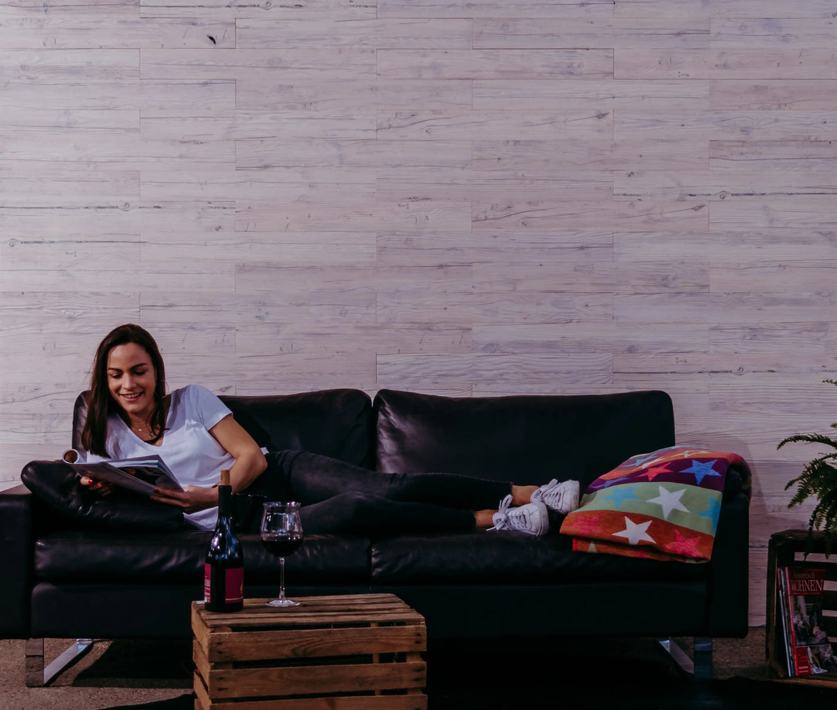 Frau liegt auf einem Ledersofa vor einer Wand aus Holzpaneelen im Design “Eis”
