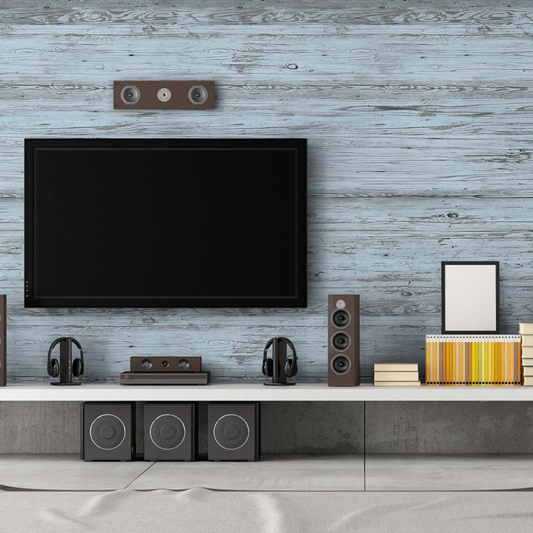 Ein moderner Heimkino-Bereich mit einem großen Flachbildfernseher vor einer Akzentwand aus hellblauen Holzpaneelen in Vintage-Optik. Die technische Ausstattung mit Lautsprechern auf einem weißen Sideboard harmoniert mit dem rustikalen Charme der Wandverkleidung.
