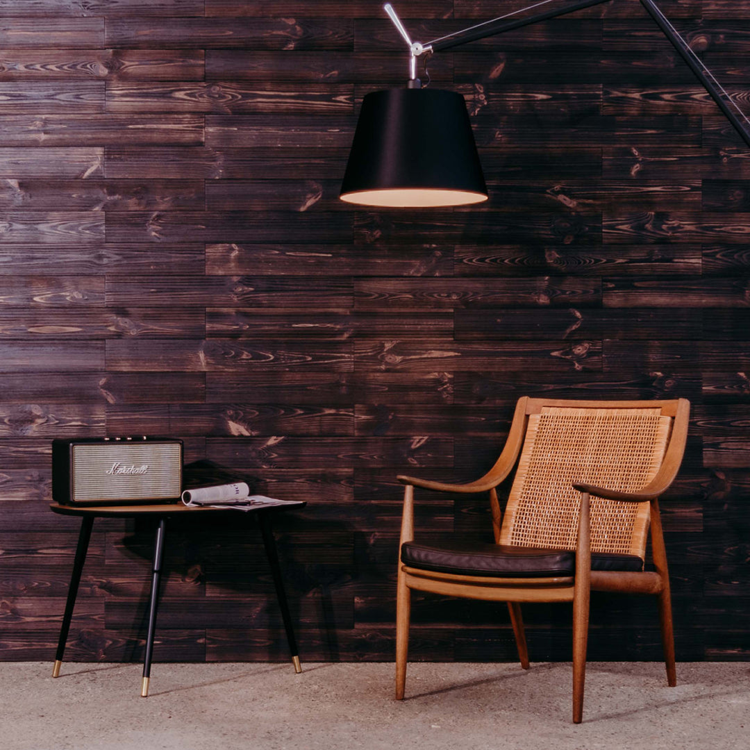 Ein stilvoller Leseplatz mit einem Retro-Sessel aus Geflecht und Leder vor einer Wand aus dunkelbraunen Holzpaneelen. Ein kleiner Beistelltisch mit Musikbox und eine große schwarze Bogenlampe schaffen eine elegante Loft-Atmosphäre.