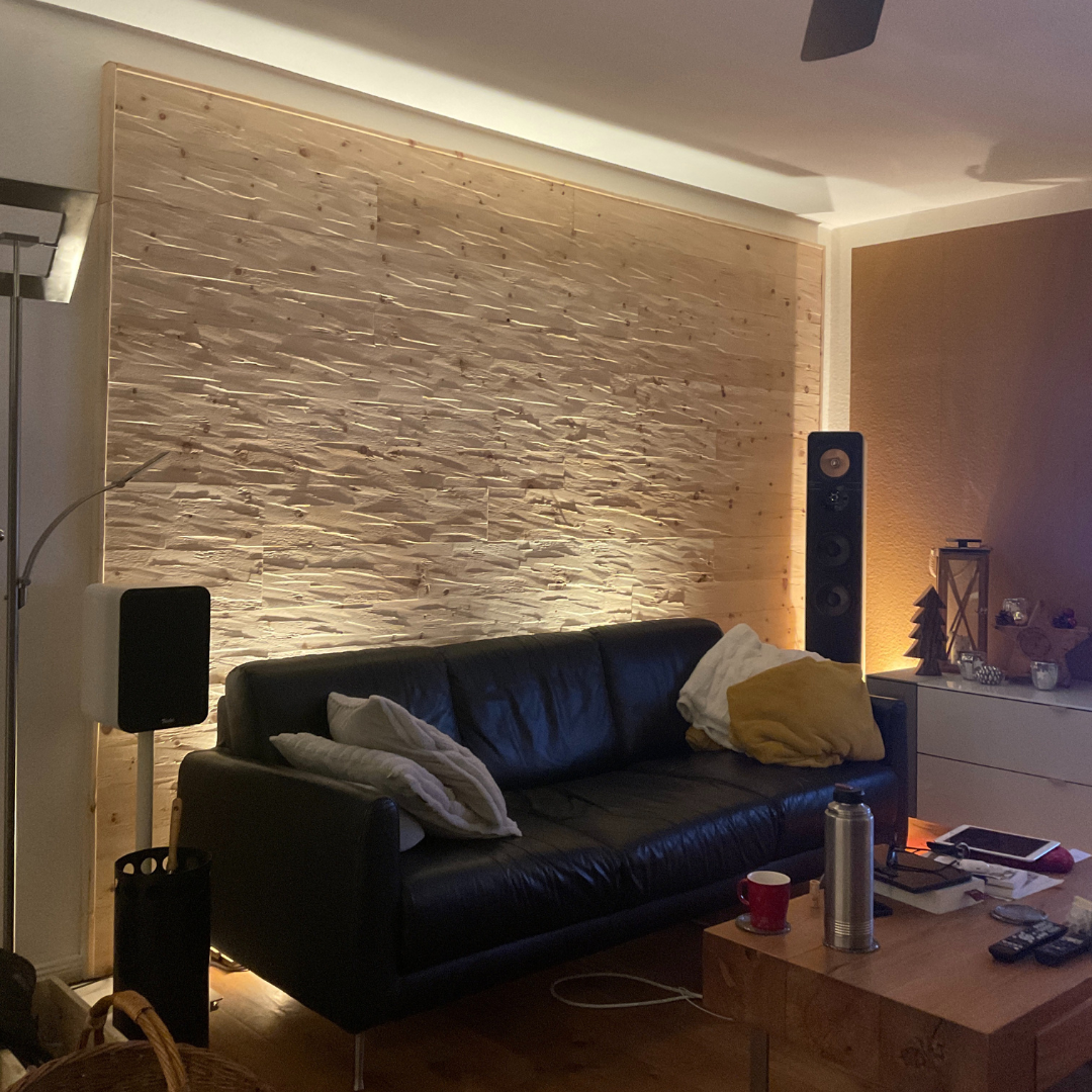 Wohnzimmerwand mit Tiroler Zirbe Paneelen vor der ein Sofa steht