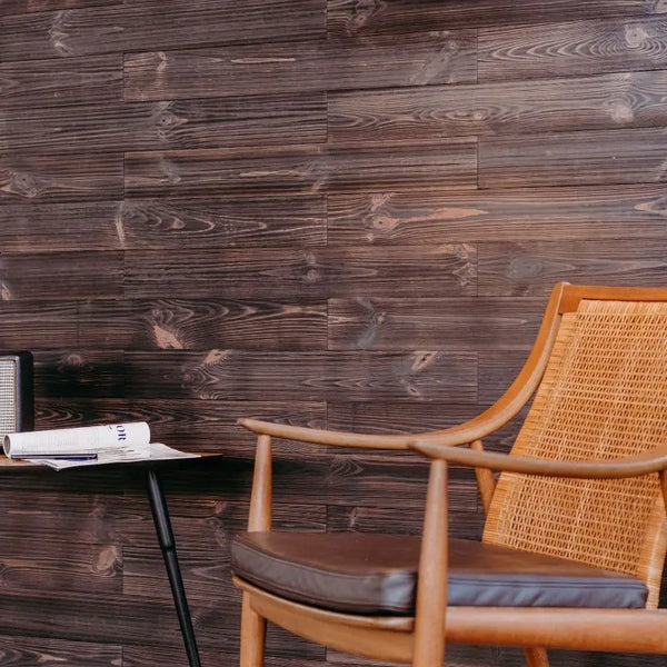 Wohnzimmerwand aus Holzpaneelen im Design „Black“, davor ein Stuhl und ein Tisch mit Verstärker