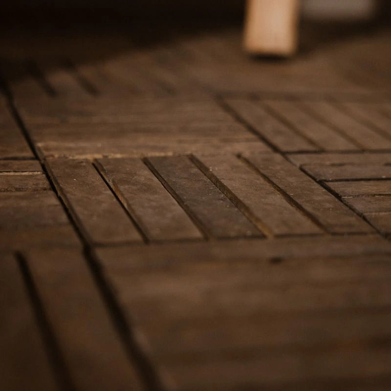 Nahaufnahme von verlegten, dunklen Holzfliesen mit feinen Rillen, die das Abfließen von Wasser ermöglichen. Die Struktur der einzelnen Holzlamellen verdeutlicht das funktionale Design für eine optimale Belüftung und Entwässerung auf dem Balkon.