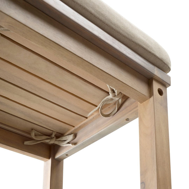 Die Detailaufnahme zeigt die Unterseite einer Sitzfläche aus Holzlatten, auf der ein beiges Sitzkissen aufliegt. Das Kissen ist mit diskreten Kordelschleifen sicher am Rahmen des Möbelstücks befestigt.