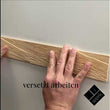 Ein Video-Vorschaubild, das die Montage einer strukturierten 3D-Wandverkleidung aus hellem Zirbenholz zeigt. Zwei Hände drücken ein Paneel an die Wand, während der eingeblendete Text „versetzt arbeiten“ auf die richtige Verlegetechnik hinweist.