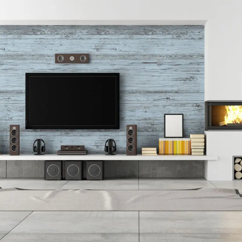 Ein modernes Wohnzimmer mit einem Flachbildfernseher und Lautsprechern vor einer hellblauen Akzentwand aus Holzpaneelen. Daneben befindet sich ein Kamin mit dekorativ aufgeschichtetem Brennholz.